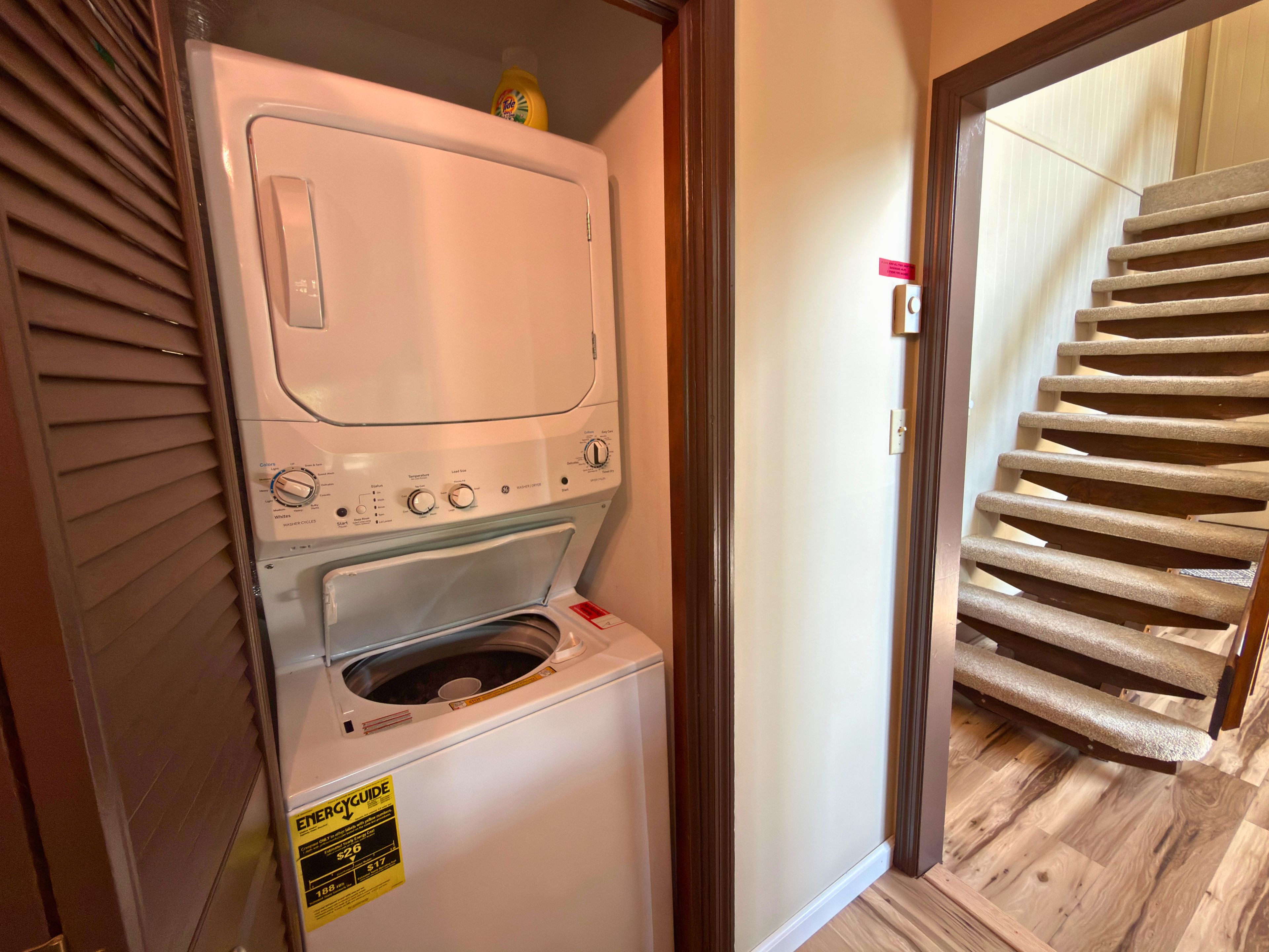 Une buanderie équipée d’un lave-linge et d’un sèche-linge à chargement frontal, d’un plancher en bois et d’un escalier menant à un autre niveau.