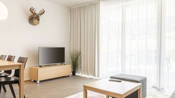 A modern living room with a flat-screen TV, a dining table with chairs, a sofa, and a decorative deer head on the wall.