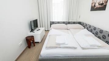 A hotel room with a bed, a TV on a nightstand, a wooden stool, and a painting on the wall.
