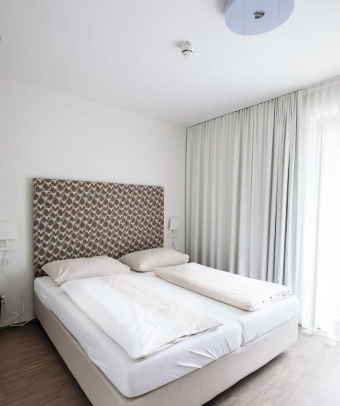 Quarto moderno com cabeceira estampada, cama grande com lençóis brancos e janela com cortinas.