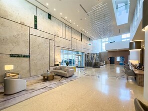 Een ruime lobby met een hoge plafond, modern meubilair en een groot raam dat natuurlijk licht binnenlaat.