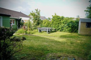 Un pati enjardinat amb un banc de fusta, una casa verda i una caseta de fusta.