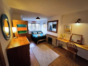 A compact room with a bed, a desk, a chair, a mirror, and a fireplace. - Ty Marlyn, St Davids (Haverfordwest)