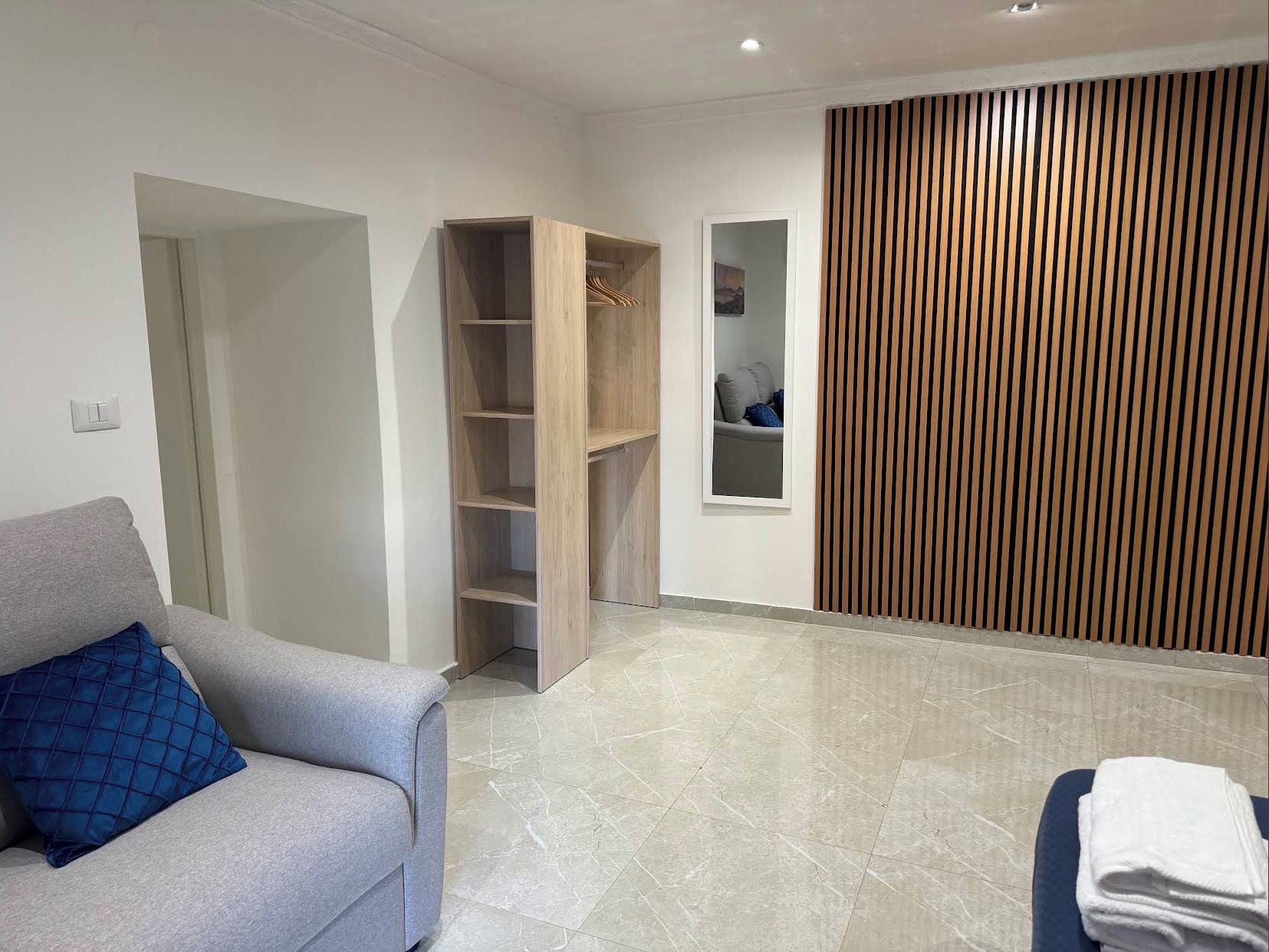 A modern room with a grey sofa, a wooden wardrobe, a built-in shelf, and a vertical wooden panel.