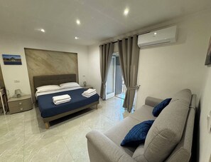 Een hotelkamer met een bed, een bank, een airconditioning en een uitzicht door een deur.