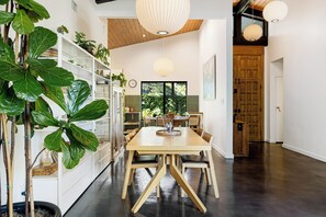 Un espace repas moderne avec une table et des chaises en bois, entouré d’étagères ornées de plantes et d’objets décoratifs.