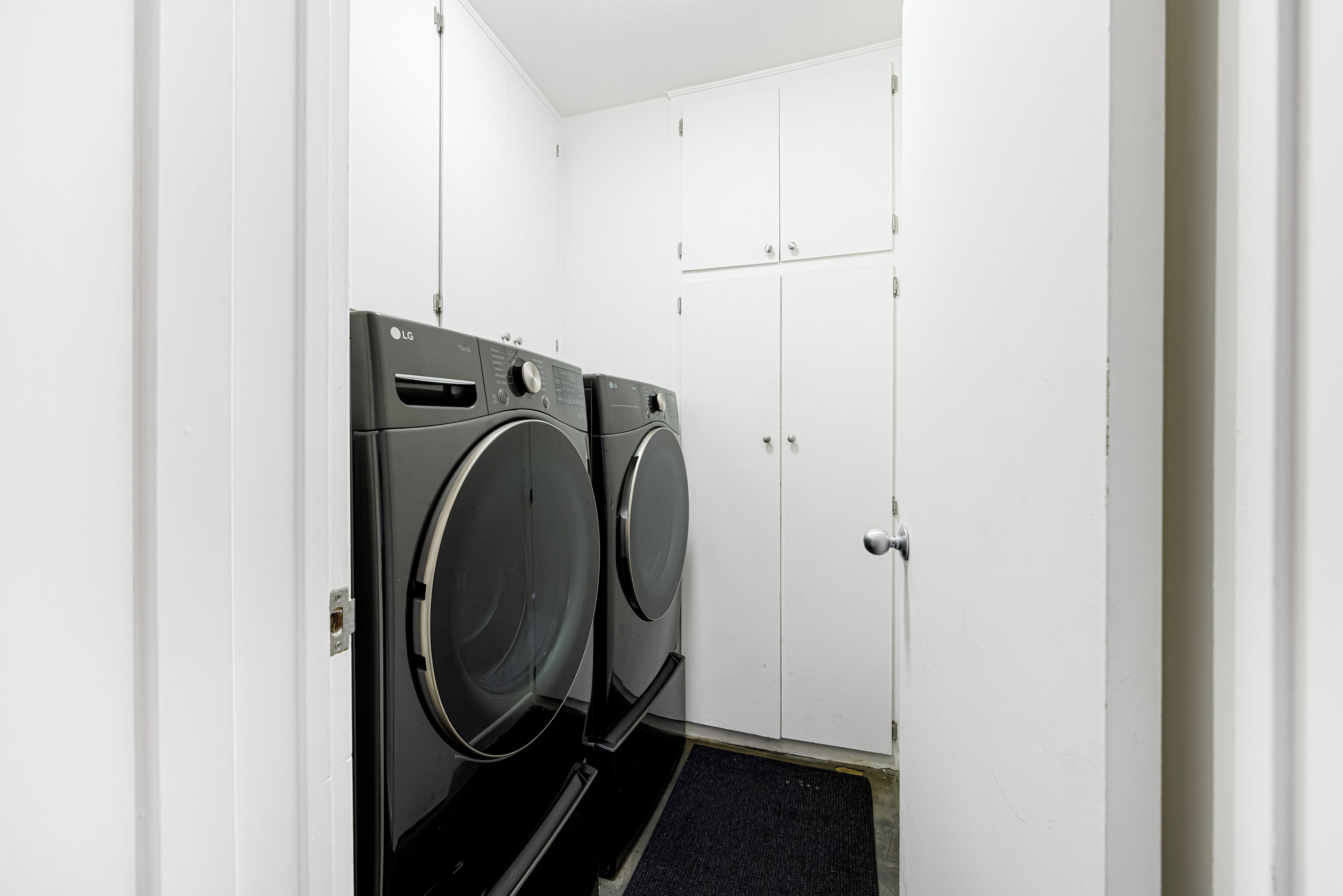 A laundry room with two LG ThinQ washing machines, white cabinets, and a door.