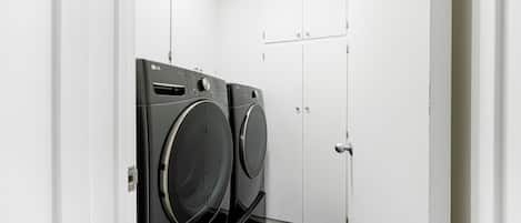 A laundry room with two LG ThinQ washing machines, white cabinets, and a door.
