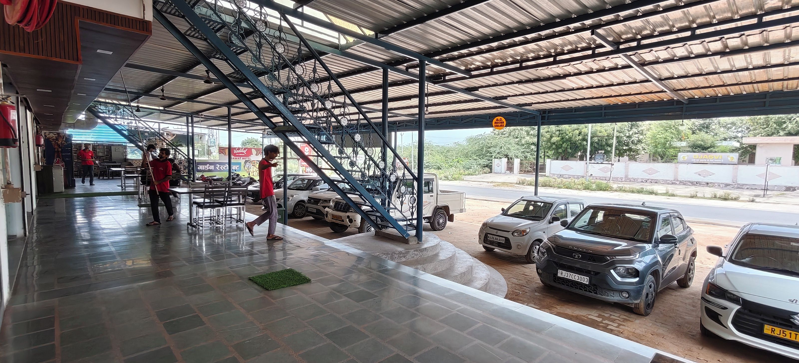 Un área de estacionamiento techada con una escalera que lleva a un nivel superior, algunos coches aparcados y una persona caminando.