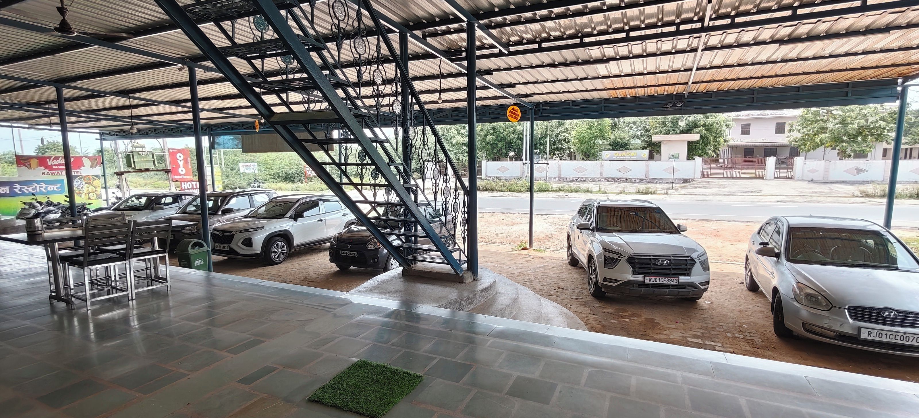 Un área de estacionamiento techada con varios coches aparcados, una escalera que lleva a un nivel superior y un letrero que indica servicio de lavado de autos.