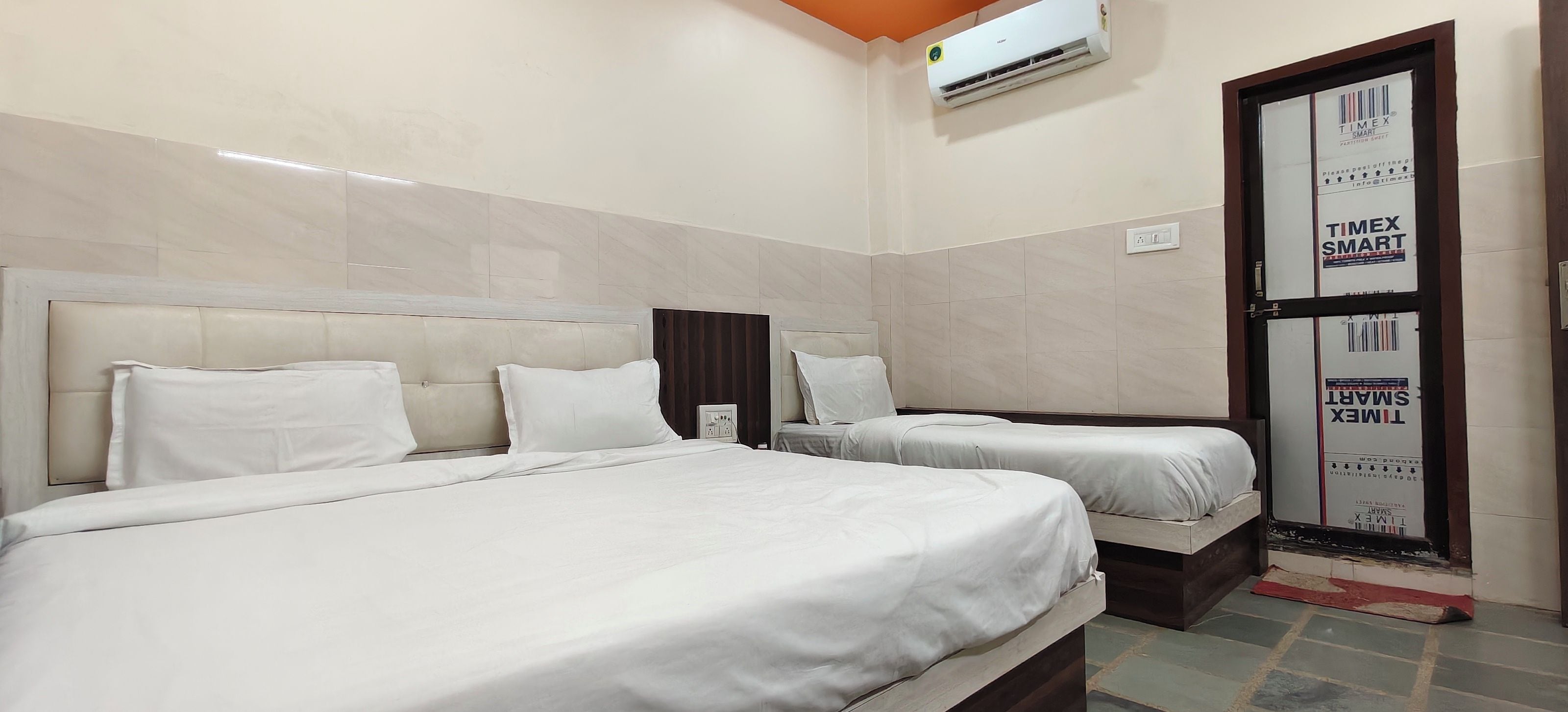 A hotel room with two beds, a minibar, and a door with Timex branding.