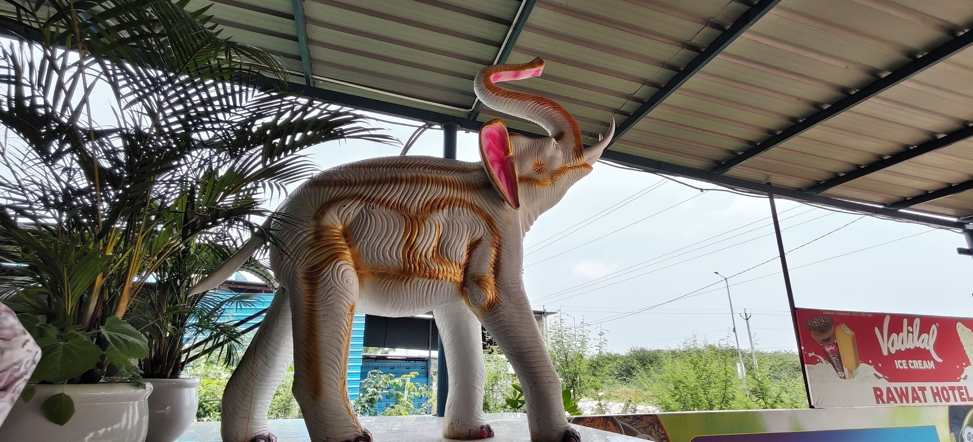 A large elephant statue under a covered area with a sign for 'Ravat Hotel' in the background.