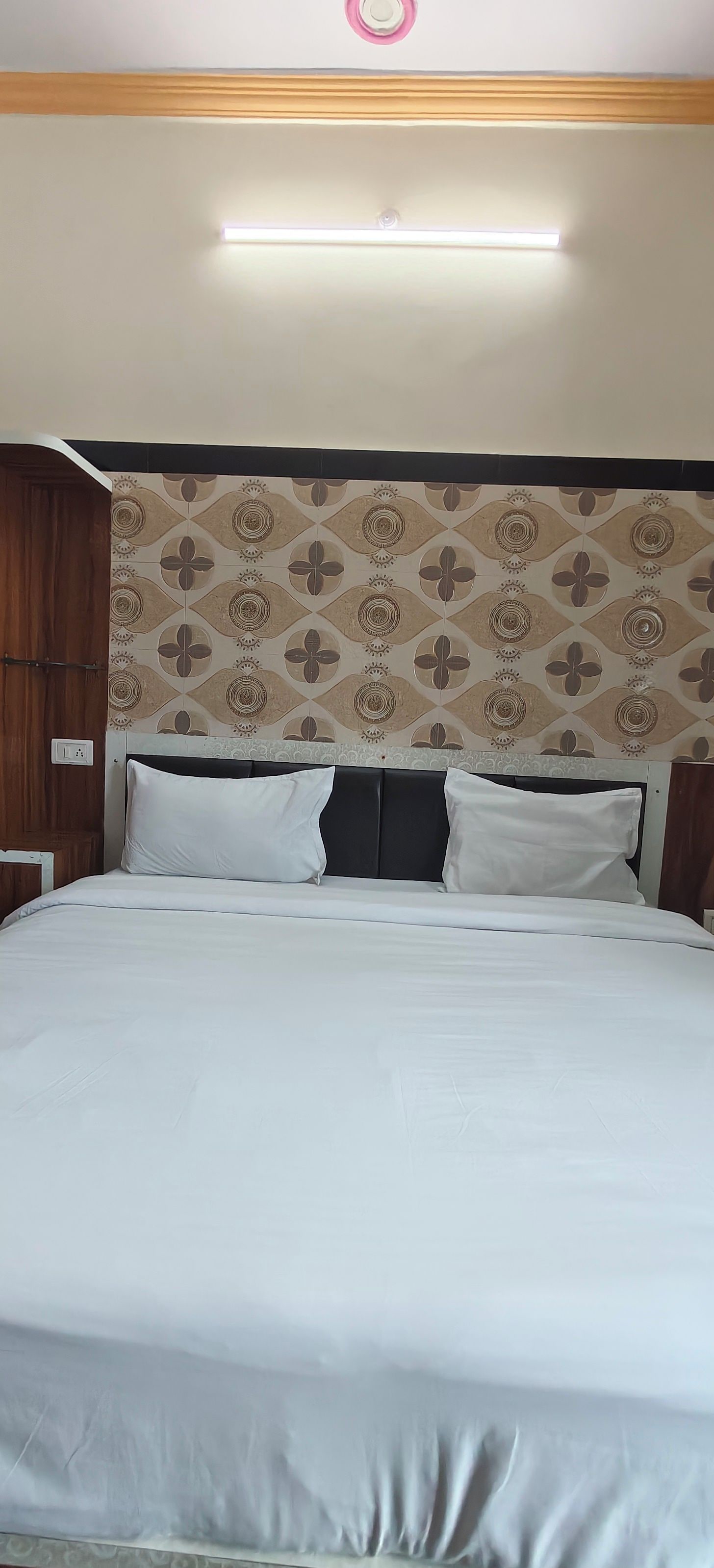 Una cama con ropa blanca, un cabecero estampado y una lámpara colgante arriba.