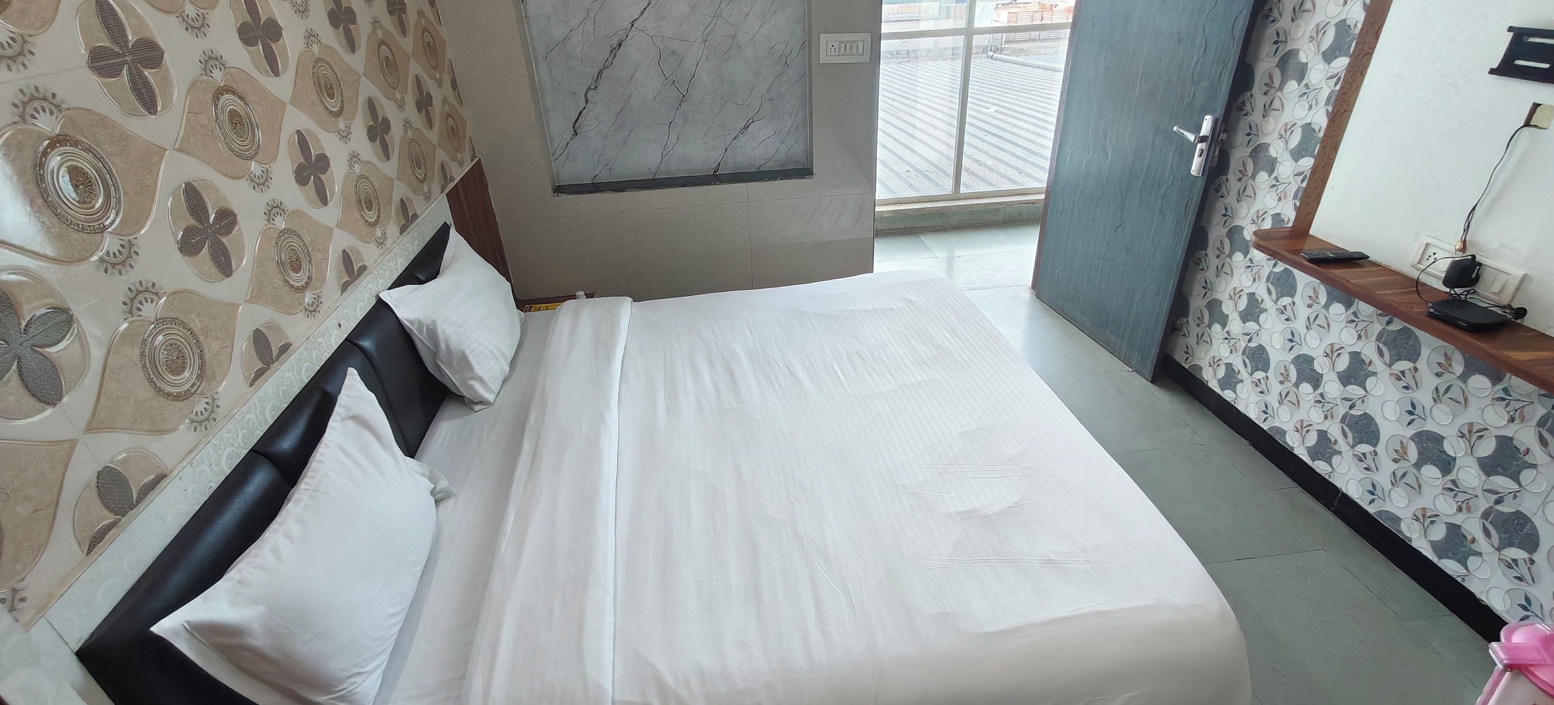 A hotel room with a bed, a window, and patterned wallpaper.
