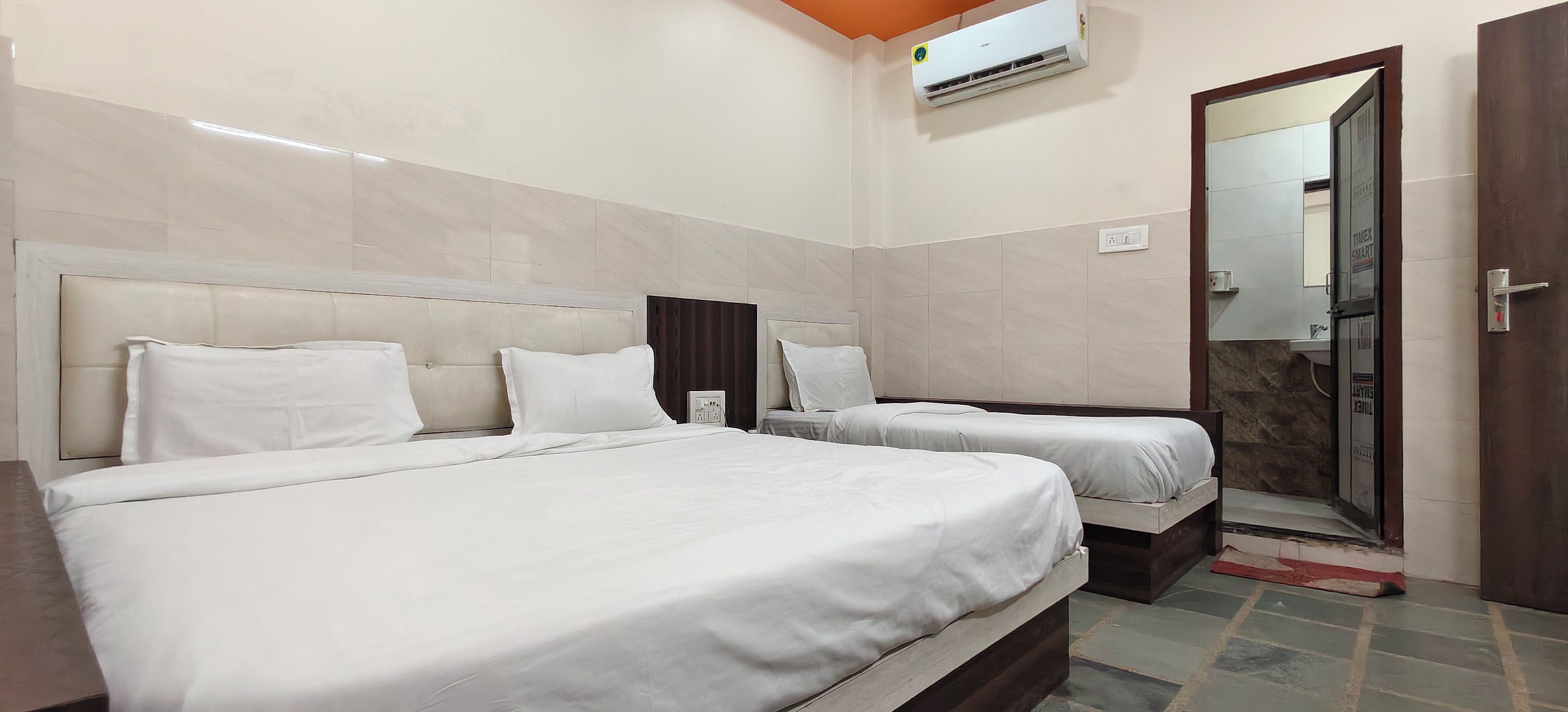 A hotel room with two beds, a large mirror, and an air conditioning unit.