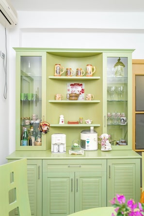 A green cabinet with shelves holding various kitchen items and a coffee maker.
