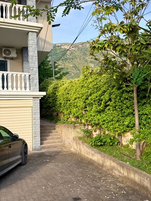 A residential building with a balcony, a car parked in front, and a staircase leading to a hillside.