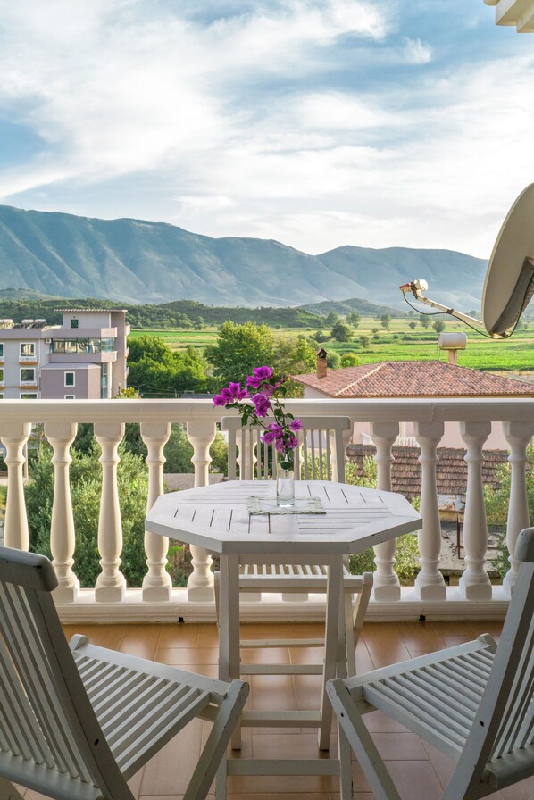 A balcony with a table and chairs, overlooking a mountainous landscape.