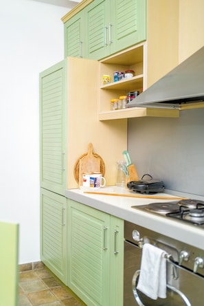 A kitchen with green cabinets, a countertop with a coffee maker, a cutting board, and a stove.