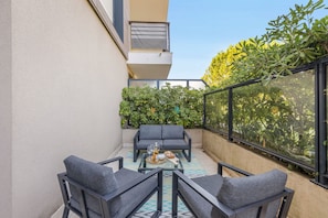 A balcony with a seating area, a glass table, and a view of greenery. - Apartment Giono by Sur la mer (Fréjus)