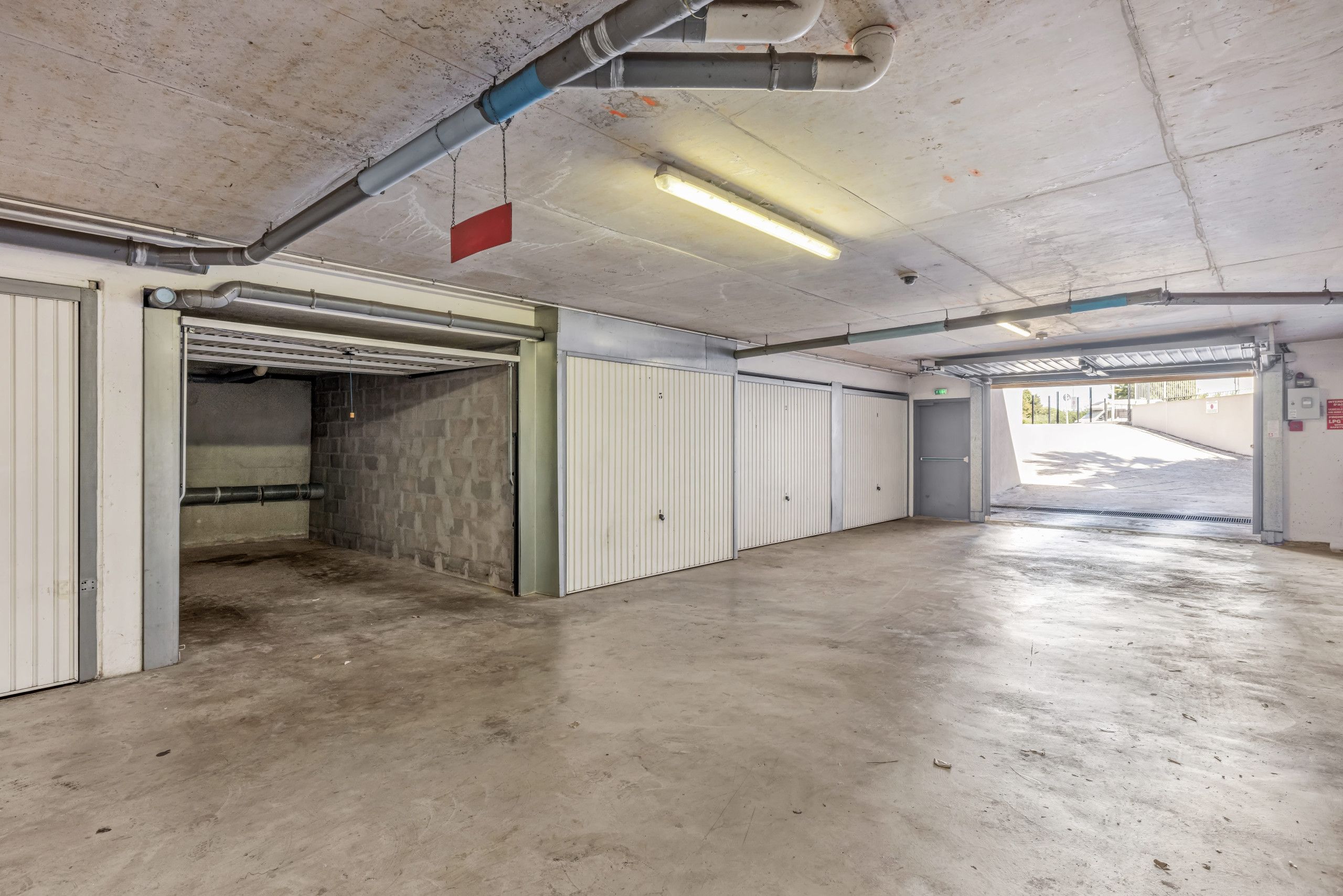 A parking garage with concrete floors, white doors, and exposed pipes.
