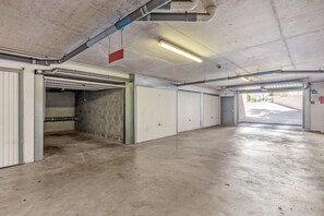 A parking garage with concrete floors, white doors, and exposed pipes. - Apartment Giono by Sur la mer (Fréjus)