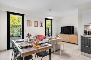 A modern kitchen with a dining area, large windows, and a flat-screen TV. - Apartment Giono by Sur la mer (Fréjus)