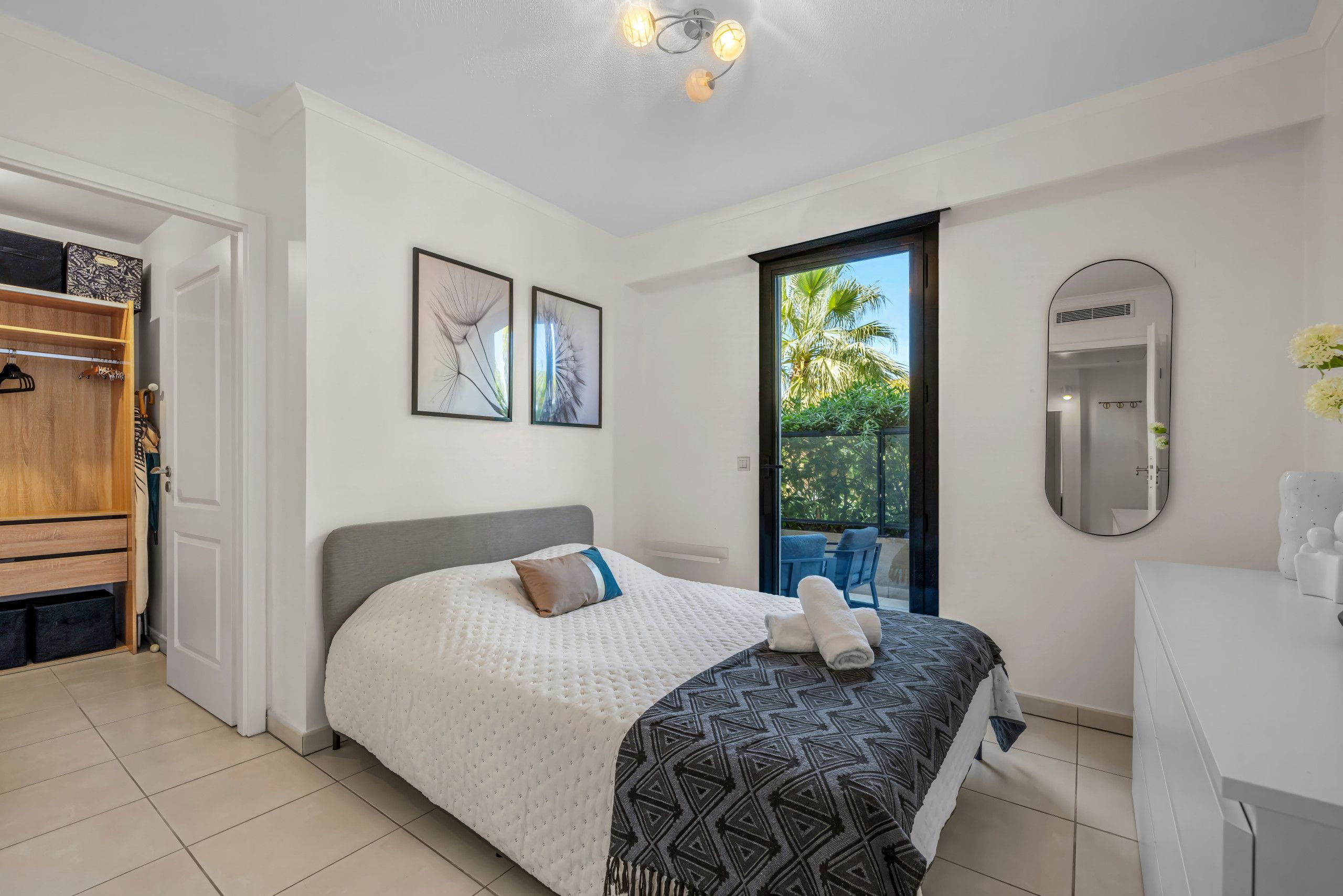 A bedroom with a bed, a wardrobe, a bathroom with a mirror, and a view of greenery outside.