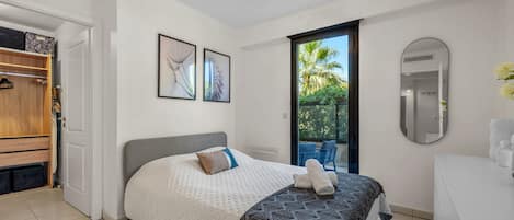 A bedroom with a bed, a wardrobe, a bathroom with a mirror, and a view of greenery outside.
