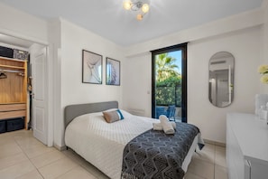 A bedroom with a bed, a wardrobe, a bathroom with a mirror, and a view of greenery outside. - Apartment Giono by Sur la mer (Fréjus)