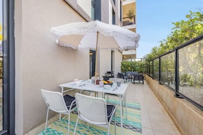 A balcony with a table set for dining, chairs, and a large umbrella. - Apartment Giono by Sur la mer (Fréjus)