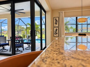 Une cuisine moderne avec une paroi en verre, un coin repas avec vue sur la piscine et un ventilateur de plafond.