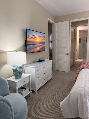 A hotel room with a bed, a desk with a lamp, a dresser, a television displaying a sunset, and a shower area. - The Golden Gator - Waterfront, Heated Pool, Lanai, Golf & Near Gulf Beaches (Rotonda West)