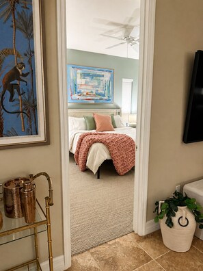 Une chambre à coucher avec un lit, un ventilateur de plafond, un tableau et un téléviseur fixé au mur.
