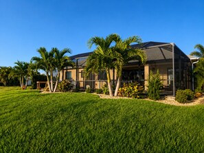 A two-story house with a covered patio area, surrounded by a well-maintained lawn and palm trees. - The Golden Gator - Waterfront, Heated Pool, Lanai, Golf & Near Gulf Beaches (Rotonda West)