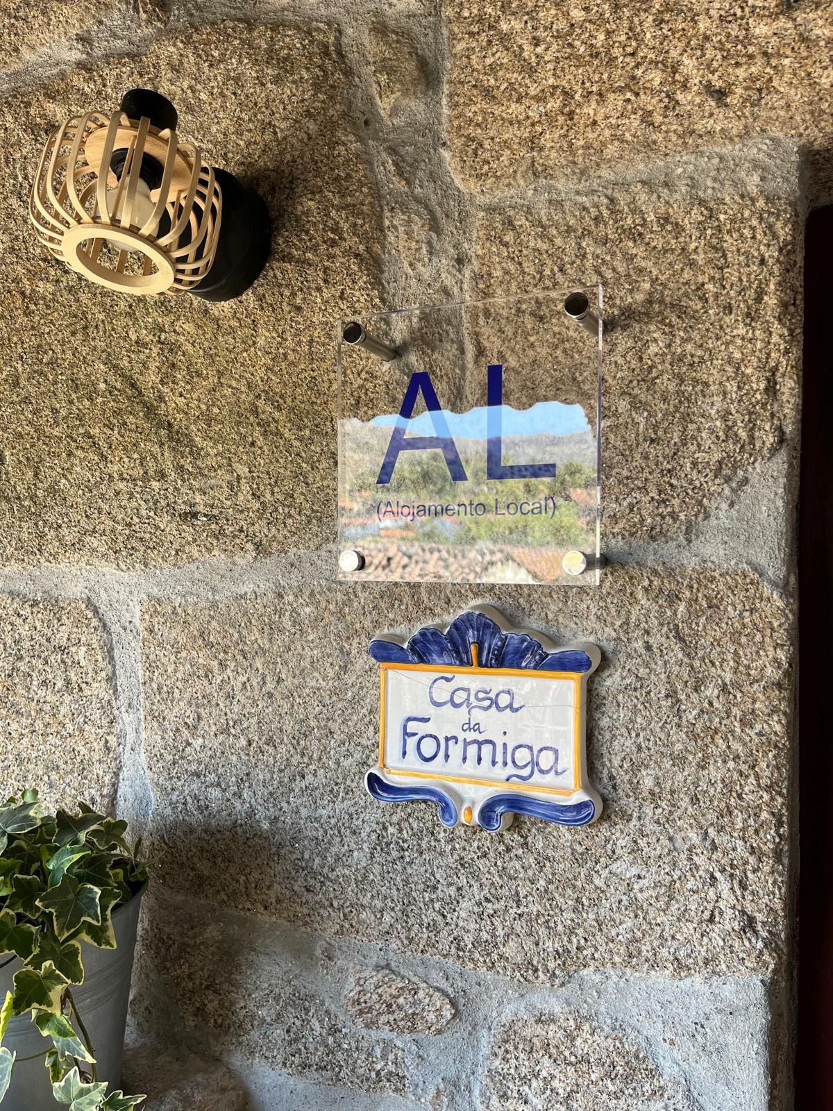 Een stenen muur met een houten lantaarn, een duidelijk bord waarop 'AL (Alojamento Local)' staat, en een keramieken huisnummer voor 'Casa da Formiga'.