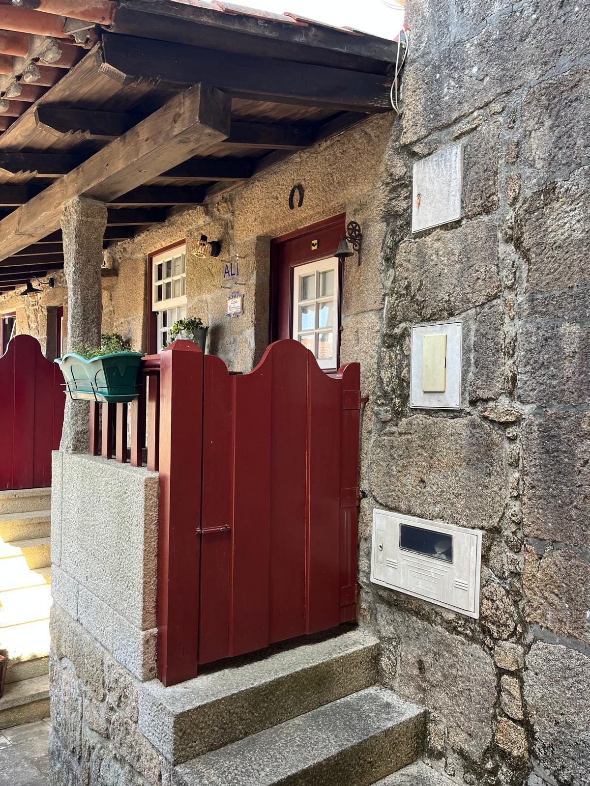 Un bâtiment en pierre avec un portail rouge, des marches menant à une porte et un petit espace porche avec une chaise verte.