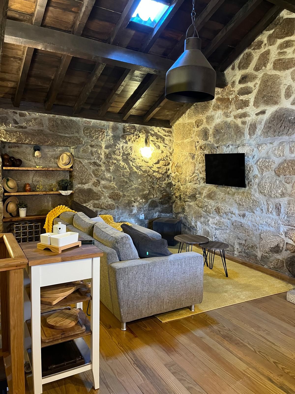 A cozy living room with a stone wall, a grey sofa, a wooden coffee table, and a television mounted on the wall.