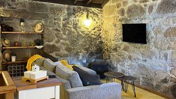 A cozy living room with a stone wall, a grey sofa, a wooden coffee table, and a television mounted on the wall.