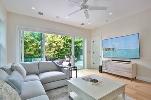 Un salon moderne avec un canapé d’angle, une table basse, un téléviseur à écran plat fixé sur un meuble en bois et un ventilateur de plafond.
