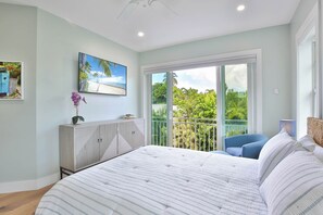 Une chambre à coucher avec un lit, une commode, un tableau et une vue sur la verdure, visible à travers une porte coulissante.