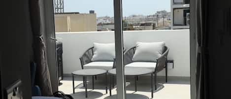 A balcony with two chairs and a small table, overlooking a cityscape.
