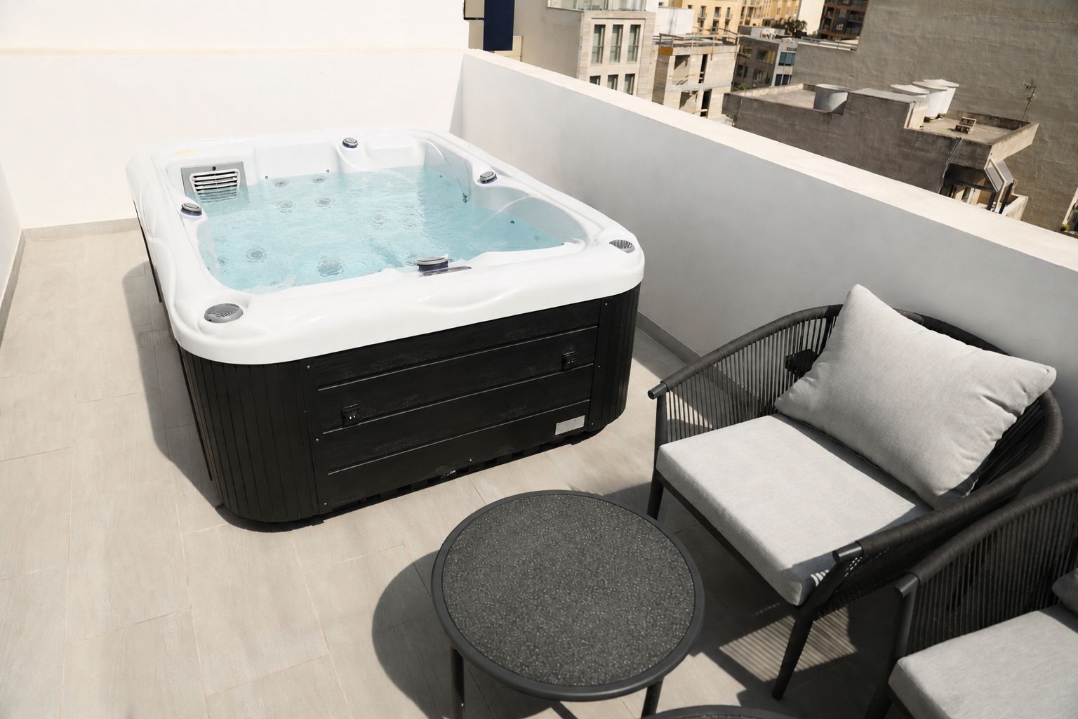 Un bain à remous sur un balcon, avec un fauteuil en osier et une petite table ronde.