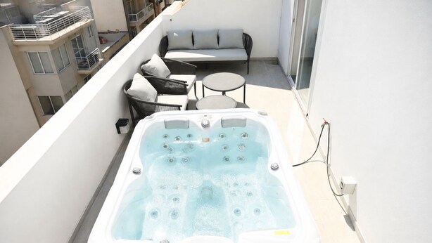 Un jacuzzi en un balcón con sofá y mesa, rodeado por un edificio.