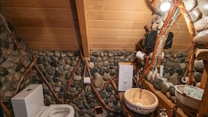 A rustic bathroom with a stone wall, wooden beams, a white toilet, and a stone basin.