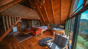 A cozy wooden cabin with a loft bedroom, a living area with a red sofa, and a view of the outdoors.