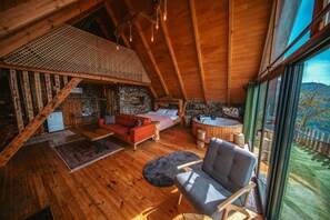 A cozy wooden cabin with a loft bedroom, a living area with a red sofa, and a view of the outdoors.