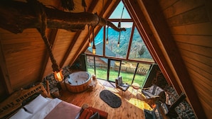 A wooden interior with a hot tub, seating area, and a view of a green landscape.