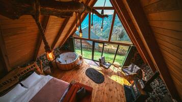 A wooden interior with a hot tub, seating area, and a view of a green landscape.