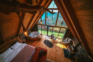 A wooden interior with a hot tub, seating area, and a view of a green landscape.